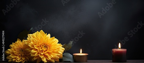 On a dark background there is a sympathy card with a burning candle and a yellow chrysanthemum nearby There is plenty of copy space around the image
