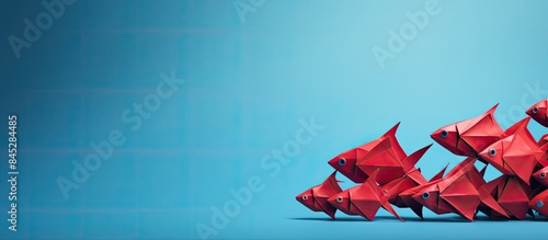A red paper origami fish sits on a white background leading a group of blue origami fish The image demonstrates the concept of leadership with space available for additional content