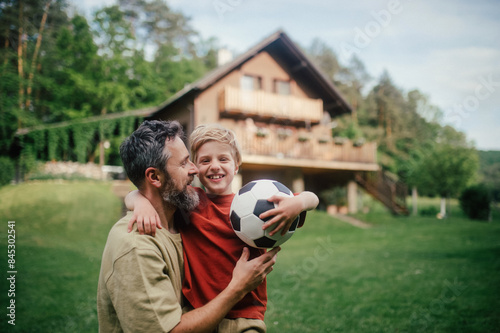 Dad embracing young son, running and celebrating the win after goal. Playing football on a lawn in front of their house. Fatherhood and Father's Day.