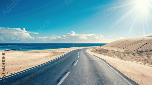 Empty highway on the background of huge sand dunes and sea coast on one side of the road, blue water, clear sunny day, bright rays, incredible nature