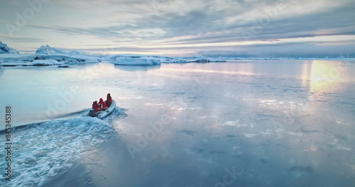 Antarctica travel and exploration, people riding motor boat. Zodiac boat sailing cold polar ocean water surface in sunset light. Discover the beauty of South Pole. Aerial winter landscape, drone