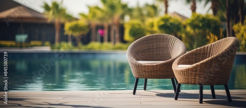 The seat lounger brown rattan chairs beside swimming pool with background is blurred of modern condominium or hotel or resort in summer day relax day. Creative banner. Copyspace image