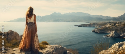 girl on a cliff looks at the sea and mountains girl in dress on nature. Creative banner. Copyspace image