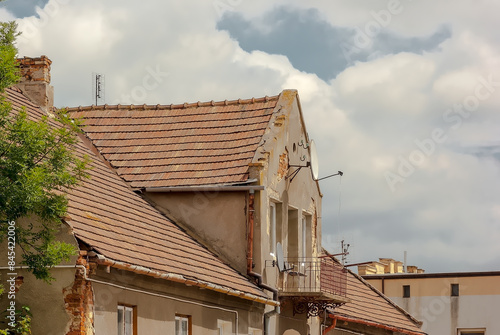 Stary ceglany dom z dachem pokrytym dachówką ceramiczną. Zabytkowy dom (lekko uszkodzony) na tle lekko zachmurzonego czerwcowego nieba.