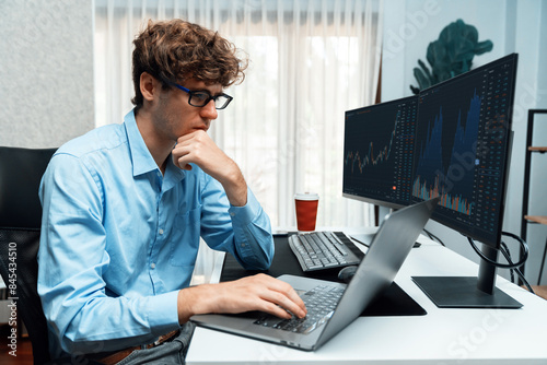 Working young business trader concentrating on laptop in market stock graph surround dynamic currency data in real time screens at modern home office, analyzing exchange rate investor concept. Gusher.