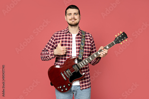 Attractive young guy playing the guitar on a pink background