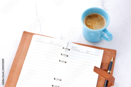 ミルクをたっぷり入れたコーヒーを飲みながら、茶色の革のシステム手帳でデスクワークをしているイメージ 