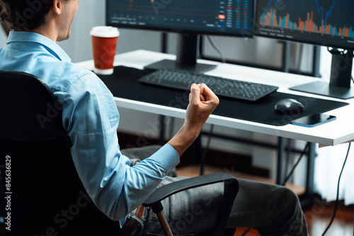 Cropped successful young stock trader calling on smartphone to business partner with dynamic financial investment screen with coffee cup on desk at modern office, trading currency theme. Gusher.