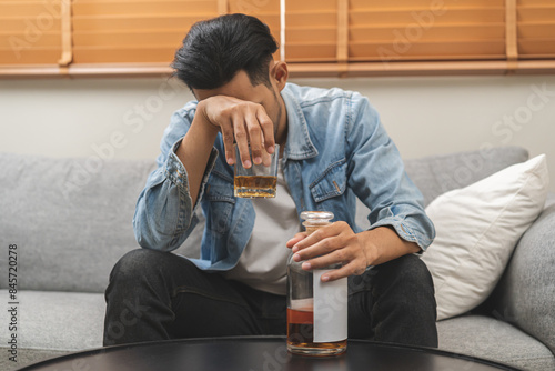 Health care alcoholism drunk, fatigue asian young man drinking beverage on table, alone depressed male drink booze on sofa at home. Treatment of alcohol addiction, suffer abuse problem alcoholism.