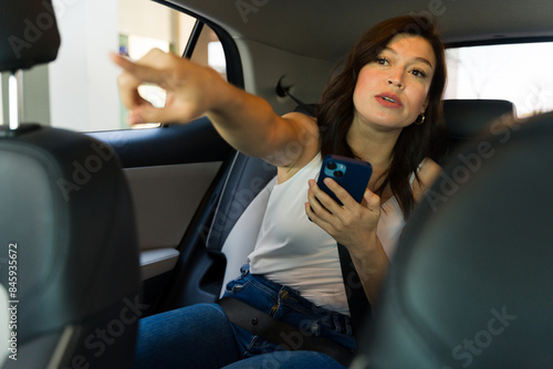 Pretty woman using her smartphone to navigate or request a stop during a ride in a modern car sharing service