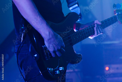 Electric bass guitar player is in blue stage lights, closeup photo