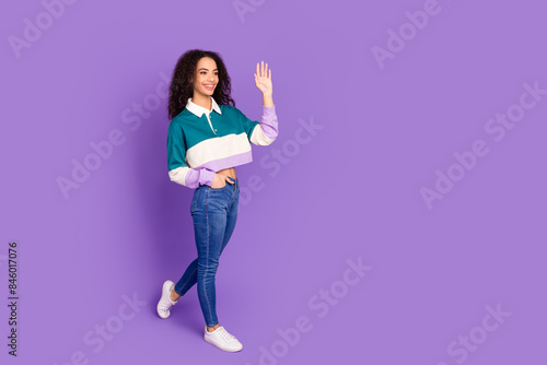 Full size photo of nice young girl walk arm wave empty space wear shirt isolated on violet color background