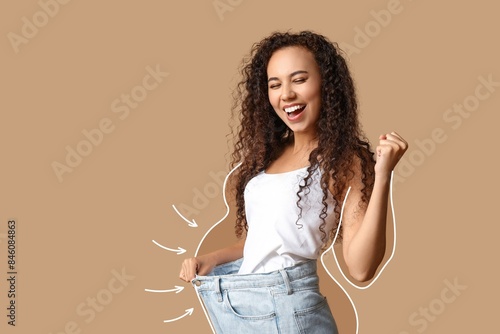 Happy young woman in loose clothes after weight loss on beige background