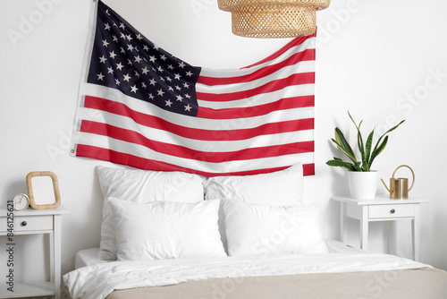 Interior of light bedroom with USA flag above cozy bed