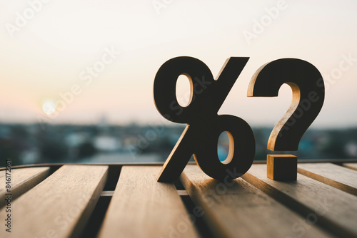 Percentage and question mark on wood table in blur urban background, raising or lowering Fed interest rates to correct inflation concepts.