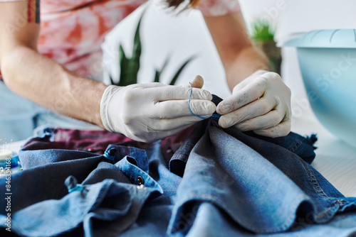 A young designer sews denim fabric in his atelier, focusing on sustainability by giving old clothing new life.