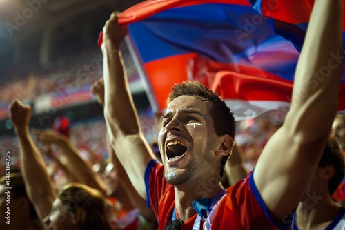 An individual in striped sports apparel rejoices with a lifted scarf against the backdrop of an illuminated stadium