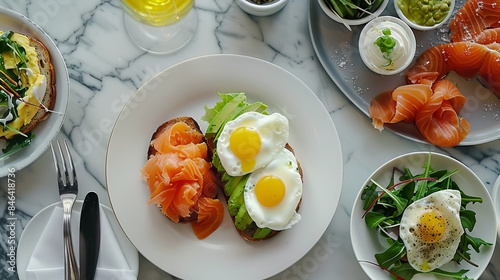 A delicious and healthy breakfast spread featuring smoked salmon, avocado, fried eggs, and fresh greens on a marble table. Healthy Breakfast with Smoked Salmon and Eggs
