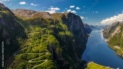 An aerial view of a winding road snaking through a lush green valley, culminating at the edge of a stunning fjord in Norway.Lysebotn, Lysefjorden, Norway