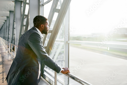 African American businessman waiting for his flight, standing by window at modern airport, copy space