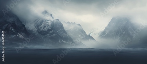 Snow-covered mountains shrouded in mist and snow under a dark, cloudy sky with a dramatic view of large peaks obscured by rain haze and low clouds, with sun rays filtering through