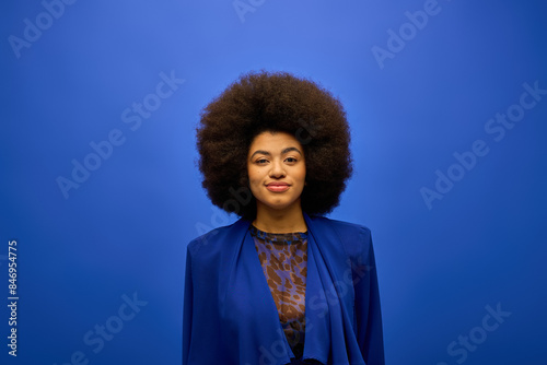 Stylish African American woman with curly hair standing confidently against a vibrant blue background.