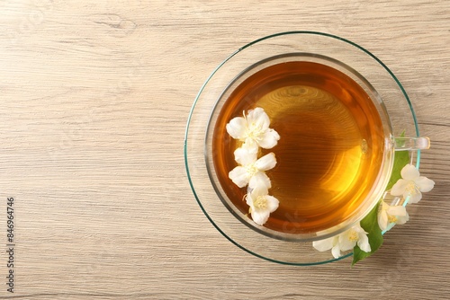 Aromatic jasmine tea in cup and flowers on wooden table, top view. Space for text