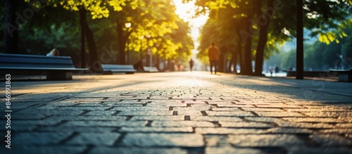 A pedestrian strolling on a sunlit city street close to a park during summertime, with a yellow and blue toned pavement view from ground level. with copy space image. Place for adding text or design