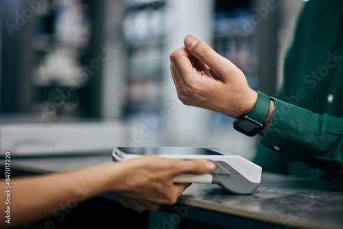 A male with a smartwatch pays his bill over it, holding it close to the payment machine at the store.