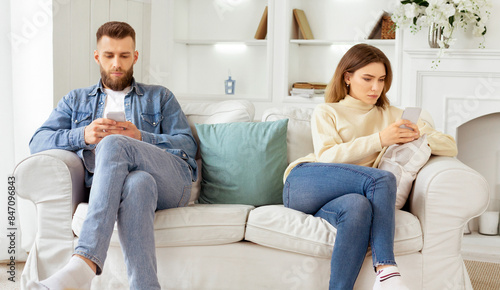 Family quarrel. Couple Staring At Their Own Smartphones, Sitting On Different Sides Of Couch