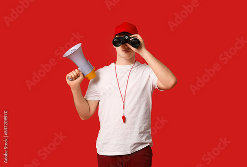 Male lifeguard with megaphone looking through binoculars on red background