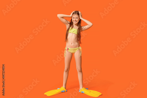 Cute little happy girl in swimsuit with flippers on orange background