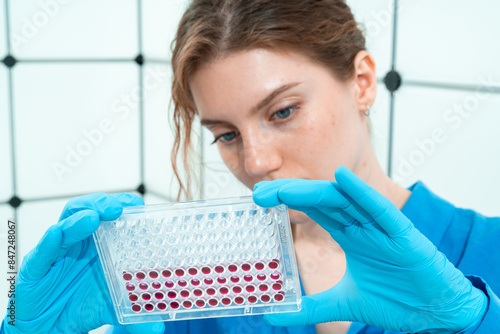 female laboratory assistant in genetics laboratory working with multi pipette and ninety-six well plate