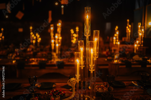 Dobele, Latvia - June 7, 2024 - Elegant candlelit dinner setting with tall glass candlesticks creating a warm and intimate ambiance. Blurred background with dining tables. Copy space.