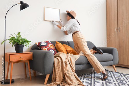 Female spy examining hanging frame on wall in room