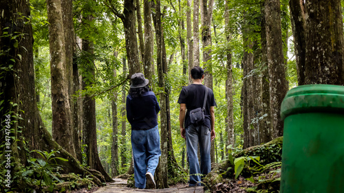 Rear view of asian couple walking together on a pathway in green lush thick forest in Aiknyet, Lombok, Indonesia. Relaxing in nature, recreation, freedom.