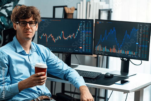 Profile of young stock trader with curly hair sitting against on dynamic financial exchange trading data screen while holding coffee up. Concept of professional business digital investment. Gusher.