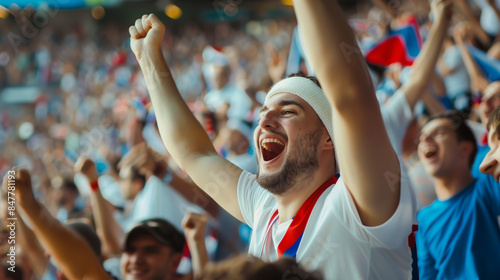 Excited football fans in a stadium celebrating a scored goal at an important game, all dressed in the colors of their national team.