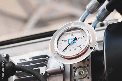 Industrial pressure gauge with white dial and blue numbers located on an industrial compressor or machine conveyor