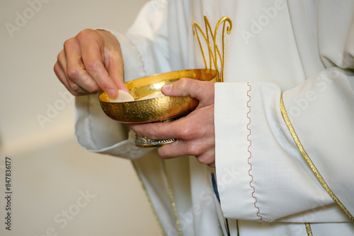 Priest wearing a white alb with golden ornaments, holding a golden chalice with consecrated hosts during a mass celebration