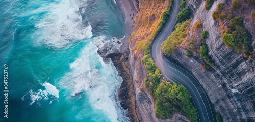 Aerial shot of a coastal road hugging the shoreline, with waves crashing on one side and cliffs on the other, captured in vibrant detail.