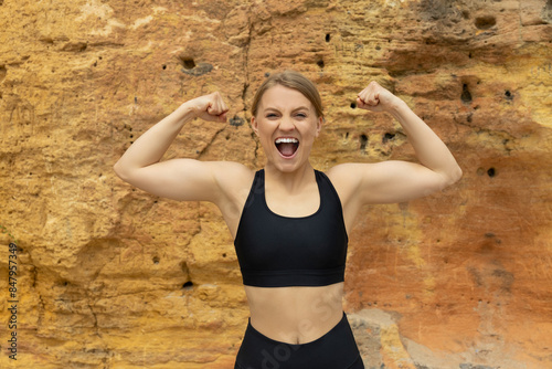 Young strong woman in sportswear screams on rock
