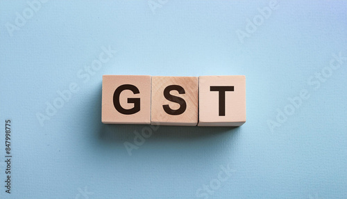 Wood blocks with abbreviation text GST - Goods and services tax. Blue backdrop. Top view