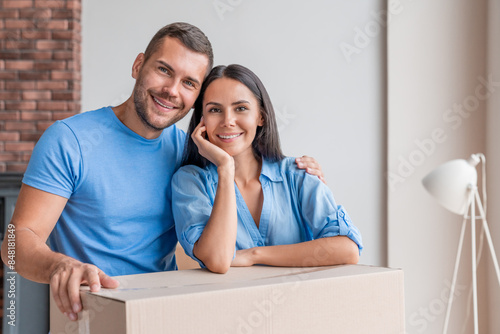 Portrait of bonding happy wife and husband moved in new house. Smiling family of two leaning on cardboard boxes in own apartment. Mid adult couple hugging embracing in their new home. House ownership.