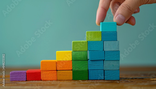 Hand placing wooden blocks in ascending order to form a colorful staircase