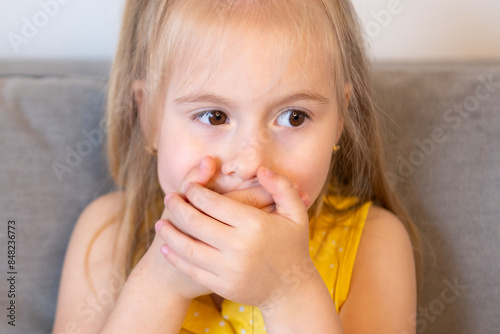 sweet child 5 years old, shy blonde girl covered mouth with hands, struggle to keep secret and maintain self-discipline, control difficulties, Mind your words
