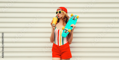 Summer stylish relaxed modern young woman with skateboard drinks fresh juice in colorful clothes