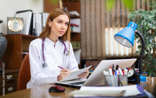 Experienced young woman therapist working with case histories on laptop in modern office