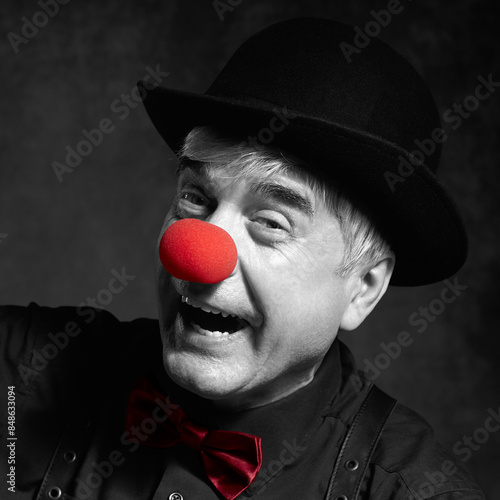 Selective color portrait of laughing clown. Dressed in black shirt with suspenders, red clown nose and bowler hat on head