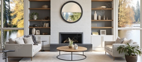Stylish living room with built in cabinets a round mirror above a grey tile fireplace a tufted sofa two armchairs and a window wall showing a view of nature Located in the Northwest USA Includes copy